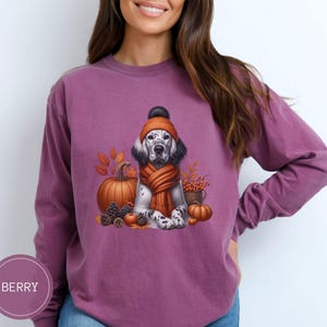 May include: A purple long-sleeved t-shirt with a graphic of a dog wearing a knitted hat and scarf, surrounded by fall leaves, pumpkins, and a basket of berries.