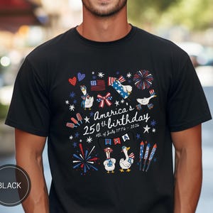 May include: Black t-shirt featuring a patriotic design for America's 250th birthday. The graphic includes cartoon geese, fireworks, and flags, with the text "America's 250th birthday 4th of July 1776-2026". The shirt has a crew neck.