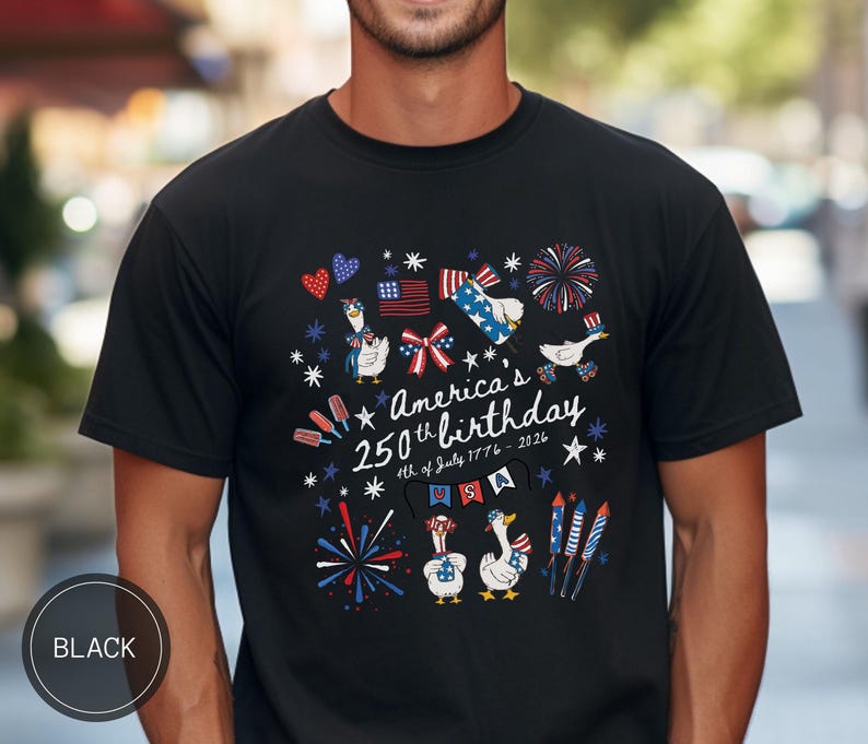 May include: Black t-shirt featuring a patriotic design for America's 250th birthday. The graphic includes cartoon geese, fireworks, and flags, with the text "America's 250th birthday 4th of July 1776-2026". The shirt has a crew neck.
