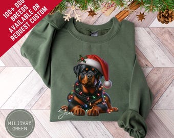Może przedstawiać: Zielona wojskowa bluza z psem rasy Rottweiler w czapce Świętego Mikołaja i lampkami choinkowymi. Bluza ma napis "100+ DOG BREEDS AVAILABLE OR REQUEST CUSTOM" i imię "Sam".