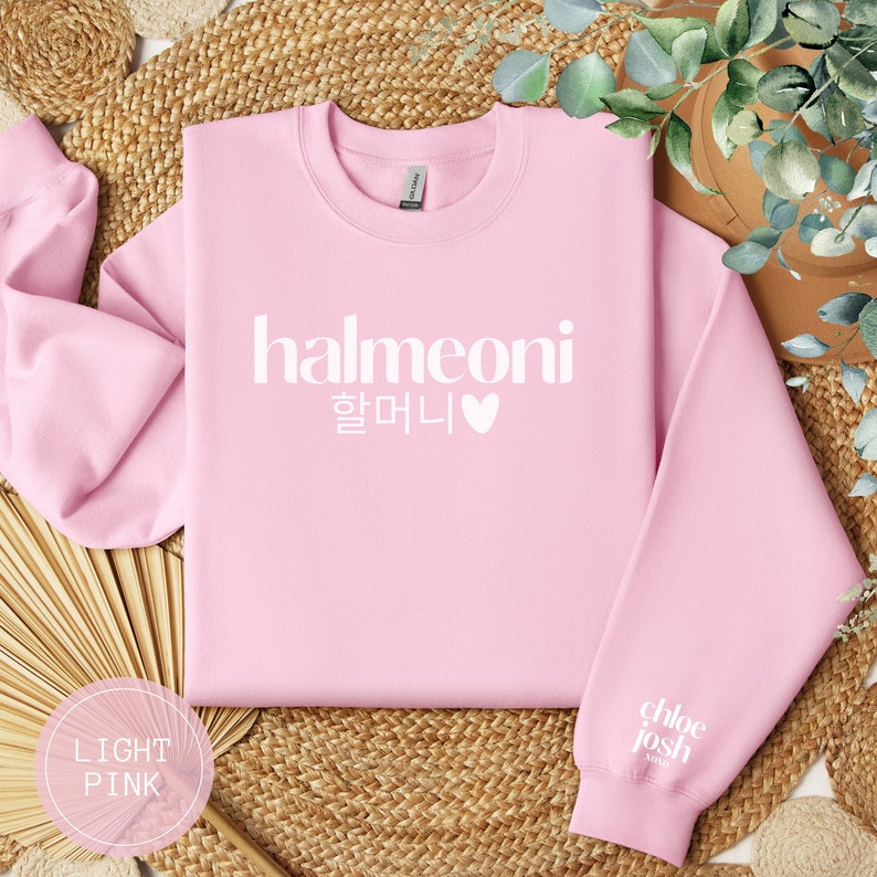 May include: Light pink sweatshirt with the text "halmeoni 할머니" and a white heart on the front. The sweatshirt has a white tag on the back of the neck that says "chloe josh" and "made" in white text.