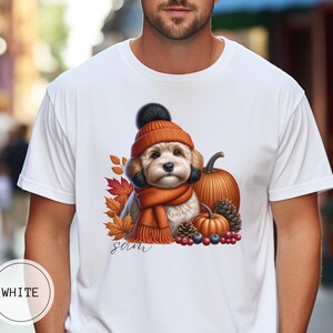 Könnte beinhalten: Weißes T-Shirt mit einem Aufdruck eines Hundes, der einen braunen und orangen Hut und Schal trägt, umgeben von Herbstblättern, Kürbissen und Beeren. Der Text "Sam" ist unter dem Aufdruck gedruckt.