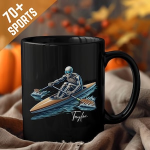 Puede incluir: Taza de cerámica negra con un esqueleto practicando kayak sobre agua azul. El esqueleto lleva gafas azules y rema en un kayak de madera. La taza tiene el texto "70+ SPORTS" y el nombre "Taylor".