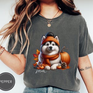May include: A gray t-shirt with a cartoon image of a husky dog wearing a scarf and a pumpkin hat. The dog is surrounded by fall leaves and pumpkins. The text "sam" is printed below the dog.