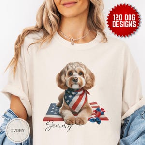 May include: Ivory t-shirt featuring a graphic of a dog wearing a red, white and blue bandana and sitting on a red, white and blue American flag. The dog's name, "Sammy", is written in cursive below the dog.