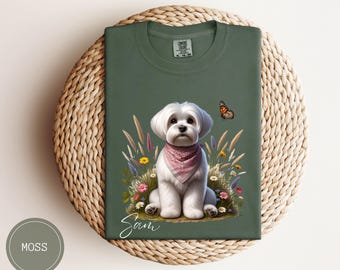 May include: A green t-shirt with a white Maltese dog wearing a pink bandana and a butterfly on a green background. The text "Sam" is printed on the shirt.