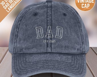 May include: A blue denim baseball cap with white embroidered text that reads "DAD EST 2025".