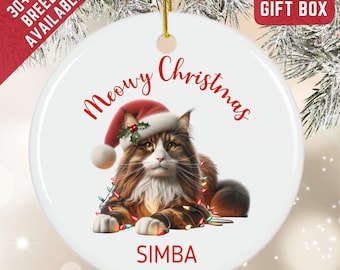 May include: A round white ceramic ornament featuring a brown and white long-haired cat wearing a red Santa hat with a sprig of holly. The cat is wrapped in colorful Christmas lights. The text reads Meowy Christmas and the name SIMBA.