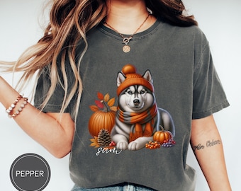 May include: A gray t-shirt with a graphic of a husky dog wearing a fall-themed hat and scarf. The dog is surrounded by pumpkins, leaves, and berries. The text "Sam" is printed below the dog.