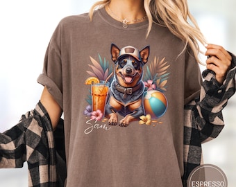 May include: A brown t-shirt with a graphic of a blue heeler dog wearing a hat and sunglasses, a tropical drink, and a beach ball. The text "Sam" is printed below the graphic.