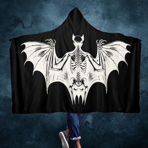 May include: Black hooded blanket with a white skeleton bat design. The bat has large wings and a skeletal body.