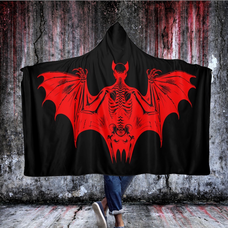 May include: A black hooded blanket with a red skeleton bat design. The bat has large wings and a skeletal body.