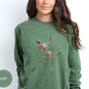 May include: Green long-sleeve sweatshirt featuring a skeleton figure pole dancing. The skeleton is in a dynamic pose, with arms and legs extended. The word "HEMP" is printed on a green circle in the lower left corner.
