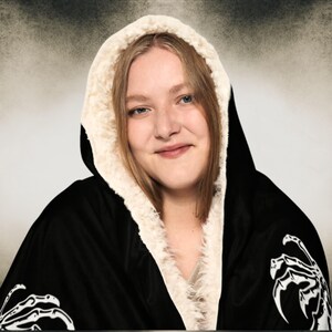 May include: Black hooded blanket with a white sherpa lining and a skeleton hand design.