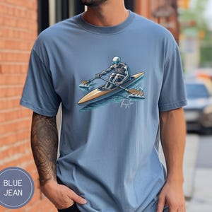Puede incluir: Una camiseta azul con un gráfico de un esqueleto remando un bote. El gráfico incluye el texto "Taylor".