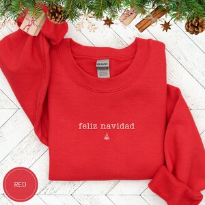 May include: A red crewneck sweatshirt with the text "Feliz Navidad" and a small Christmas tree graphic. The sweatshirt is made of a soft material and is perfect for the holiday season.