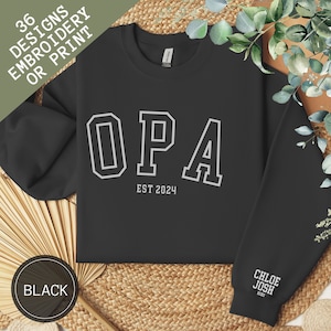 Peut inclure: Sweat-shirt noir avec un texte blanc qui dit "OPA EST 2024". Le sweat-shirt a un motif brodé blanc sur la manche qui dit "CHLOE JOSH XOXO".
