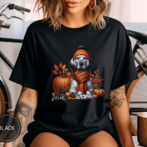 May include: Black t-shirt with a graphic of a dog wearing a hat and scarf with pumpkins and fall leaves. The text "Sam" is printed on the shirt.