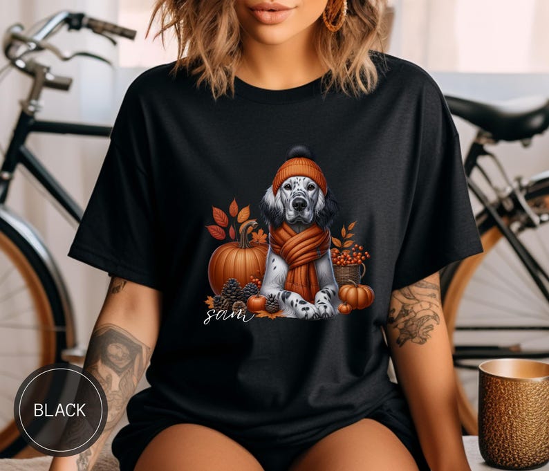 May include: Black t-shirt with a graphic of a dog wearing a hat and scarf with pumpkins and fall leaves. The text "Sam" is printed on the shirt.