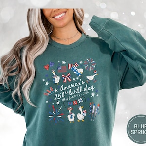 May include: A teal sweatshirt featuring a patriotic design for America's 250th birthday. The graphic includes fireworks, flags, and cartoon geese. The text reads "America's 250th birthday 4th of July 1776 - 2026".