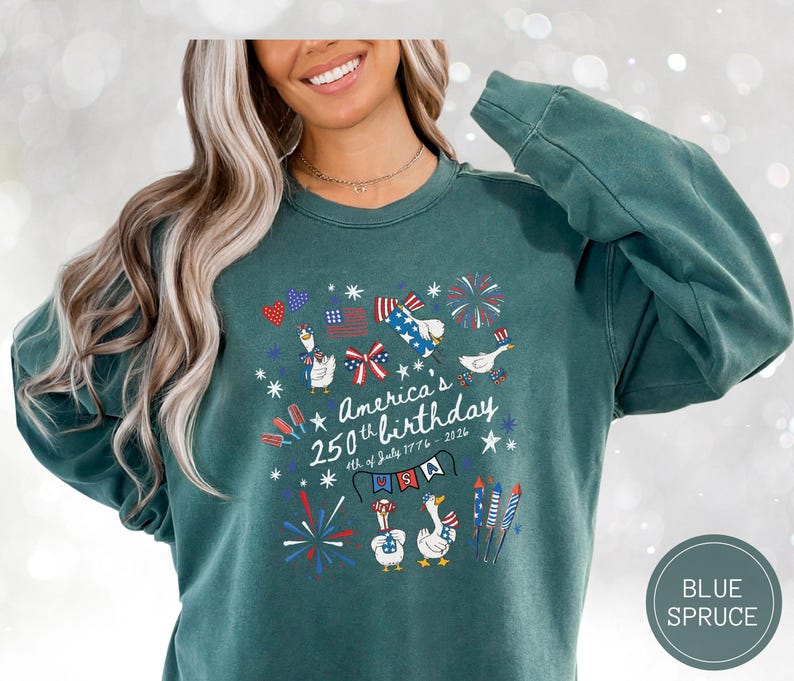 May include: A teal sweatshirt featuring a patriotic design for America's 250th birthday. The graphic includes fireworks, flags, and cartoon geese. The text reads "America's 250th birthday 4th of July 1776 - 2026".
