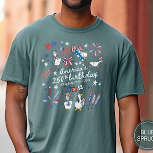 May include: A blue spruce t-shirt featuring a graphic commemorating America's 250th birthday. The design includes fireworks, patriotic geese, and the text "America's 250th birthday 4th of July 1776-2026" in red, white, and blue.