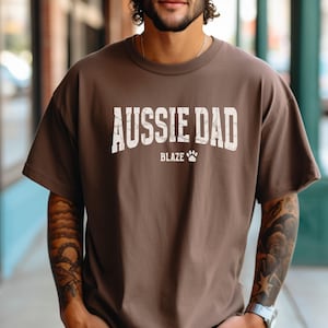 May include: A brown t-shirt with the text "Aussie Dad" in white with a paw print and the word "Blaze" underneath.
