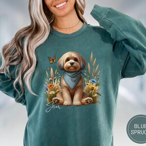 Può includere: Una felpa blu turchese con una grafica di un cane marrone e bianco che indossa un bandana e circondato da fiori. Il testo "Sam" è stampato sotto il cane.