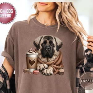 Puede incluir: Camiseta color espresso con una ilustración de un perro Mastín, una taza de café, macarons y una magdalena. La camiseta tiene el texto "170+ DOG BREEDS" en un diseño circular. El perro está envuelto en una bufanda marrón.