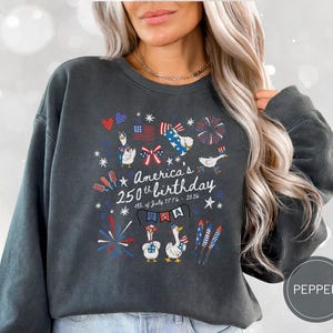 May include: Dark grey sweatshirt featuring a patriotic design for America's 250th birthday. The design includes fireworks, flags, and cartoon geese. Text reads "America's 250th birthday 4th of July 1776-2026".