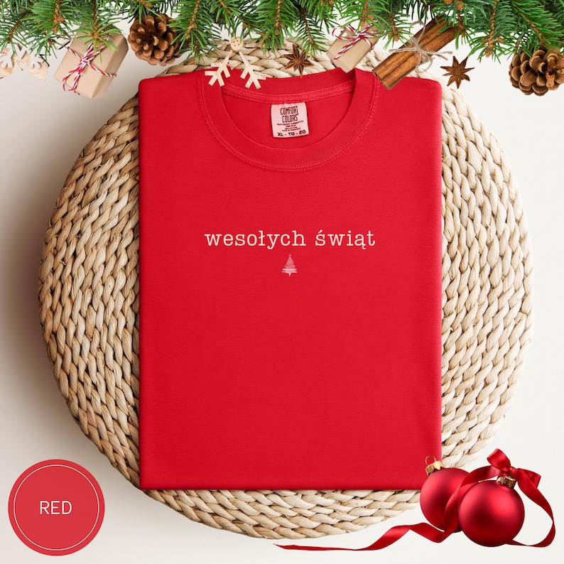 Może przedstawiać: Czerwony t-shirt z kr&oacute;tkim rękawem z białym napisem wesołych świąt oraz małą białą ikoną choinki wyśrodkowaną na klatce piersiowej. Koszulka posiada okrągły dekolt oraz metkę marki Comfort Colors nadrukowaną po wewnętrznej stronie kołnierza.
