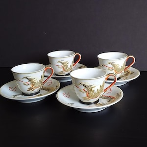May include: Set of four white porcelain teacups and saucers with a gold and red dragon design.