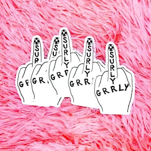 Könnte beinhalten: Weiße Aufkleber mit schwarzer Umrandung, die eine Hand zeigen, die den Mittelfinger zeigt. Das Wort "SURLY" steht vertikal auf dem Mittelfinger, und "GRR" oder "GRRLY" steht auf den Knöcheln. Der Hintergrund ist eine flauschige rosa Textur.