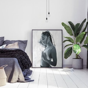 May include: Black and white painting of a woman with long braids, wearing a white vest top and looking down. The painting is framed and hanging on a white wall.