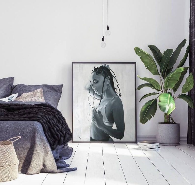 May include: Black and white painting of a woman with long braids, wearing a white vest top and looking down. The painting is framed and hanging on a white wall.