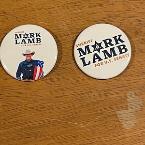 May include: Two white round campaign buttons with a blue star and the text "Sheriff Mark Lamb for U.S. Senate". One button features a photo of a man in a cowboy hat and a sheriff's badge.