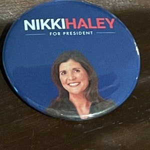 May include: A round, blue button with the text "NIKKI HALEY FOR PRESIDENT" in white and red. The button features a portrait of Nikki Haley.