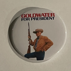 May include: A white button with a red and blue image of a man holding a rifle. The text "Goldwater for President" is printed on the button.