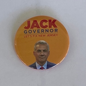 May include: A yellow button with a picture of a man and the text "JACK GOVERNOR LET'S FIX NEW JERSEY".