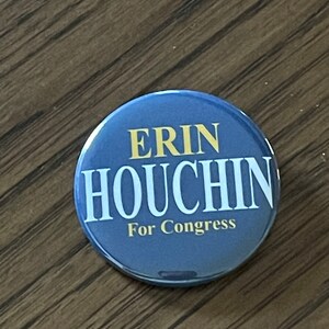 May include: A round, blue button with the name "ERIN HOUCHIN" in white letters and "For Congress" in smaller white letters. The text "ERIN" is in gold letters.