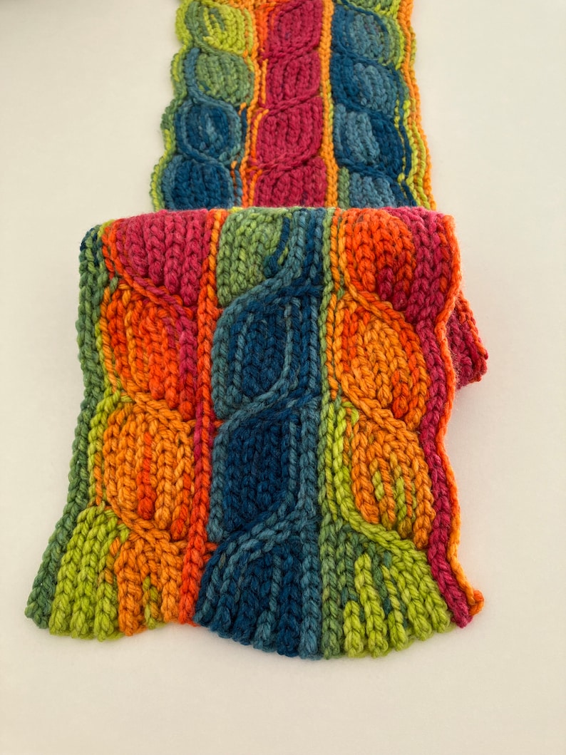 May include: A colorful knitted scarf with a cable knit pattern in shades of green, orange, red, and blue.