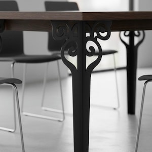 May include: A dark wood dining table with ornate black metal legs. The legs feature a decorative, swirling design. The table is surrounded by black chairs with silver legs, creating a modern aesthetic.
