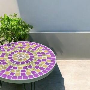 May include: A round mosaic table with a purple and gold pattern. The table is made of small square tiles and has a white base.