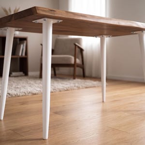 Könnte beinhalten: Ein rechteckiger Holztisch mit natürlicher Oberfläche. Der Tisch hat vier weiße, sich verjüngende Beine. Der Tisch steht in einem Raum mit Holzboden, einem Teppich und einem Stuhl. Die Tischhöhe beträgt ca. 76 cm.