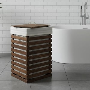 May include: A wooden laundry basket with a slatted design and a removable lid. The basket has a white fabric liner and is in a modern bathroom. The dark brown wood contrasts with the white walls and floor tiles.