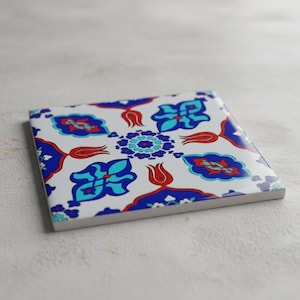 May include: Square ceramic tile with a white background and a repeating pattern of blue, red, and turquoise floral designs. The tile features a central floral medallion and corner accents.