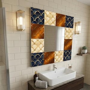 Puede incluir: Espejo decorativo cuadrado con un patrón geométrico en tonos azul marino, dorado y marrón. El espejo está colocado sobre un lavabo rectangular blanco en un baño. Dos apliques flanquean el espejo.