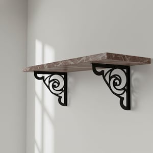 May include: A floating shelf with a marble-look top and black decorative brackets. The shelf is mounted on a white wall. The brackets have a swirling, floral design.