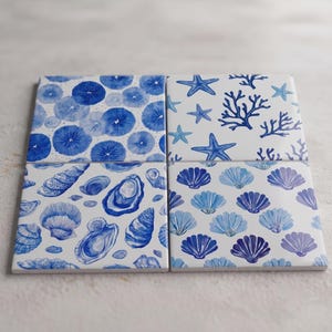 Op de afbeelding: Een set van vier vierkante keramische onderzetters met blauw-witte nautische patronen. De ontwerpen bevatten blauwe zee-egels, zeesterren met koraaltakken, diverse gedetailleerde schelpen en rijen blauwe sint-jakobsschelpen op een witte achtergrond.