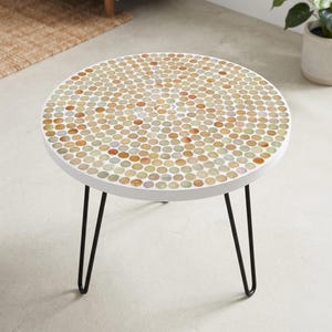 May include: A round side table featuring a tabletop covered in a dense mosaic of small, circular, translucent glass tiles in shades of amber, beige, and pale green, supported by three thin, black metal hairpin legs with a white frame.